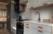 Modernes Tiny House Lodge-Küche mit weißen Schränken, Marmortheke und schicker Sitzbereich im Hintergrund.
