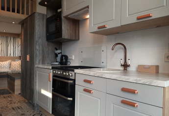 Modernes Tiny House Lodge-Küche mit weißen Schränken, Marmortheke und schicker Sitzbereich im Hintergrund.