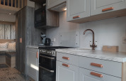 Cuisine moderne d’un lodge Tiny House avec meubles blancs, accents bois et coin salon confortable visible.
