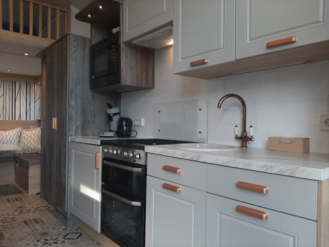 Cucina moderna in un lodge Tiny House con mobili bianchi, dettagli in legno e zona soggiorno accogliente.