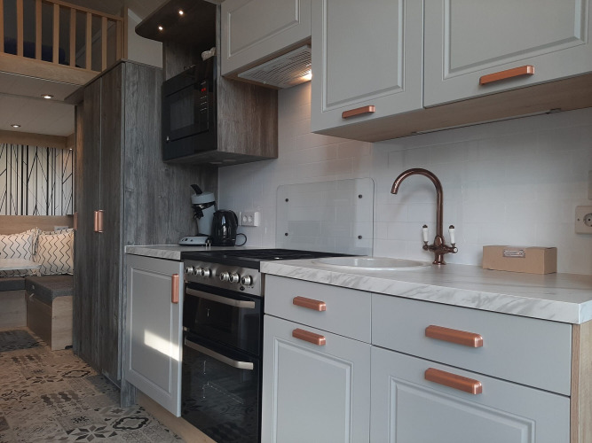 Cocina moderna de Tiny House lodge con gabinetes blancos, detalles de madera y sala de estar acogedora.