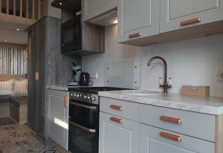 Cocina moderna de Tiny House lodge con gabinetes blancos, detalles de madera y sala de estar acogedora.