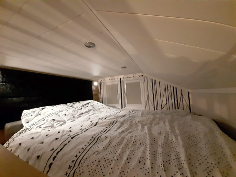 Gemütlicher Schlafbereich im Tiny House mit niedrigem Dach, gemustertem Bettbezug und dekorativer Wandgestaltung.