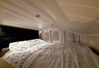 Coin nuit douillet dans le lodge Tiny house avec un plafond bas, une literie à motifs et mur de déco graphique.