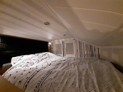 Cozy sleeping loft in the Tiny House lodge, featuring low ceilings, patterned bedding, and a unique accent wall.