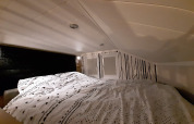 Cozy sleeping loft in the Tiny House lodge, featuring low ceilings, patterned bedding, and a unique accent wall.