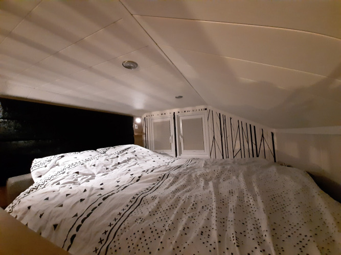 Acogedor rincón para dormir en la Tiny House, con techo bajo, ropa de cama estampada y pared decorativa.