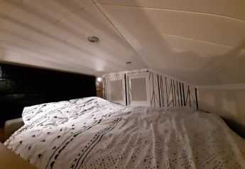 Coin nuit douillet dans le lodge Tiny house avec un plafond bas, une literie à motifs et mur de déco graphique.