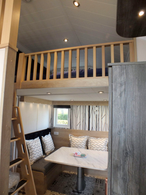 Innenaufnahme eines Tiny House Lodges mit Hochbett, Essecke, Leitertreppe und moderner Einrichtung.