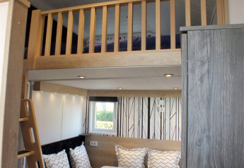 Innenaufnahme eines Tiny House Lodges mit Hochbett, Essecke, Leitertreppe und moderner Einrichtung.