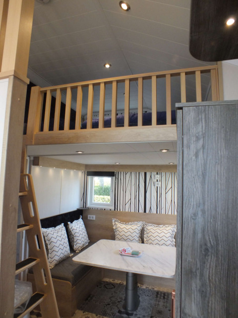 Binnenzicht van een Tiny House lodge met een verhoogd bed, eettafel, bank en moderne inrichting.