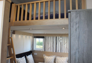 Vista interior de una casa Tiny House con altillo, mesa de comedor, sofá y decoración moderna.
