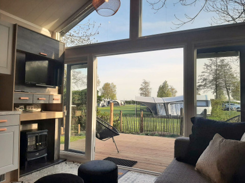 Blick aus einer gemütlichen Tiny House Lodge mit großen Fenstern auf einen Campingplatz und grüne Wiese.