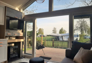 Blick aus einer gemütlichen Tiny House Lodge mit großen Fenstern auf einen Campingplatz und grüne Wiese.