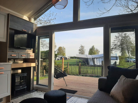Udsigt fra en hyggelig Tiny house lodge med store vinduer ud til campingplads og grønne omgivelser.