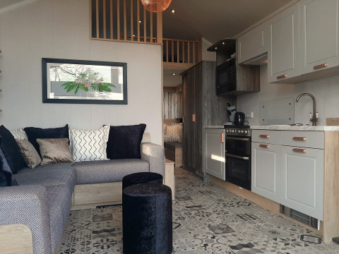 Innenraum eines Tiny House-Lodges mit gemütlichem Sofa, moderner Küche und elegant gemusterten Fliesen.