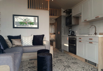 Intérieur d’un lodge Tiny House avec canapé d’angle, cuisine moderne et sol en carrelage à motifs.