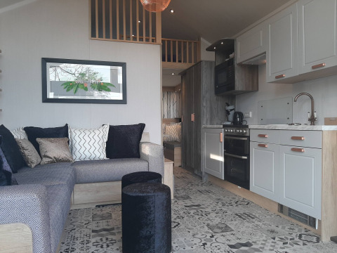 Interiør af et Tiny House-lodge med sofa, farverige puder, køkken og moderne mønstrede gulvfliser.