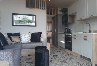 Interior de una Tiny House lodge con sofá en L, moderna cocina blanca y suelo de baldosas decorativas.