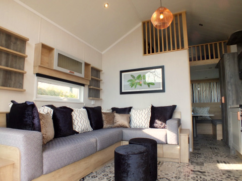 Modernes Wohnzimmer in einer Tiny House-Lodge mit gemütlichem Sofa, Kissen und Hochbett.