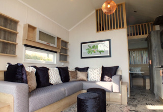 Modernes Wohnzimmer in einer Tiny House-Lodge mit gemütlichem Sofa, Kissen und Hochbett.