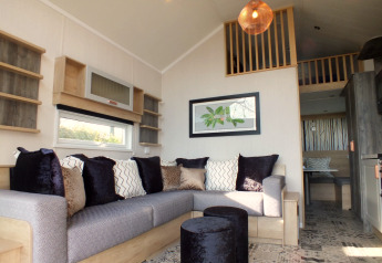 Modernes Wohnzimmer in einer Tiny House-Lodge mit gemütlichem Sofa, Kissen und Hochbett.