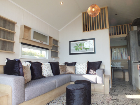 Salon moderne dans une Tiny House lodge avec grand canapé, coussins décoratifs et mezzanine.