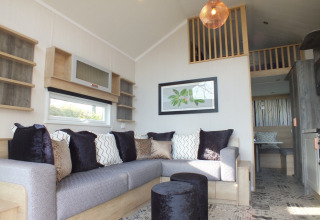 Knusse woonkamer in een Tiny House lodge met grote hoekzetel, sierkussens en een gezellige mezzanine.