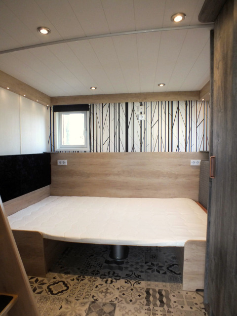 Innenraum eines Tiny House-Lodges mit modernem Bett, Holzverkleidung und gemustertem Boden.