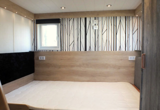 Innenraum eines Tiny House-Lodges mit modernem Bett, Holzverkleidung und gemustertem Boden.