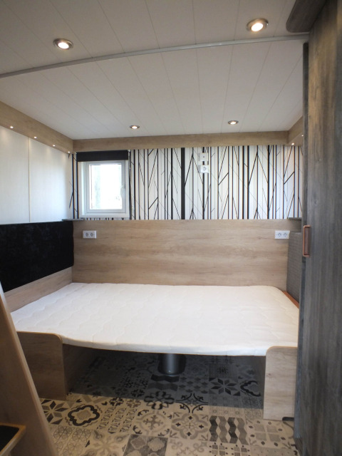 Interior view of Tiny House lodge bedroom with a modern bed, wooden panels, decorative floor tiles.