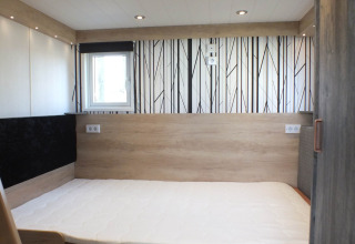 Innenraum eines Tiny House-Lodges mit modernem Bett, Holzverkleidung und gemustertem Boden.