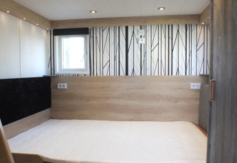 Interiør af Tiny House-lodge med moderne enkeltseng, lyst træpanel og sort-hvid vægdekoration.