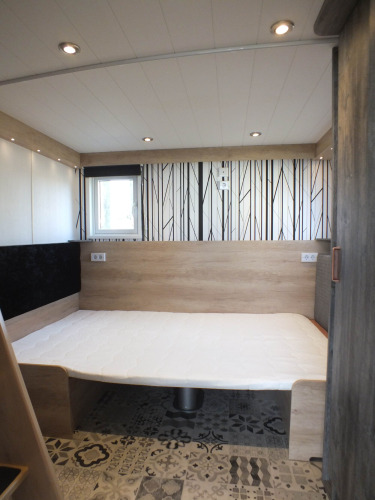 Vista interior de una Tiny House lodge con cama moderna, paneles de madera y suelo decorativo.