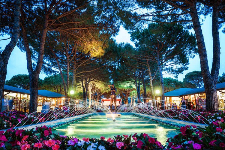 Avondfoto van fontein omringd door bloemen en bomen bij Camping Village Marina di Venezia, Veneto, Italië.