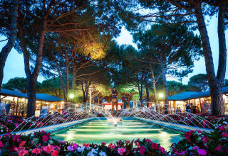 Aftenfoto af fontæne omgivet af blomster og træer på Camping Village Marina di Venezia i Veneto, Italien.