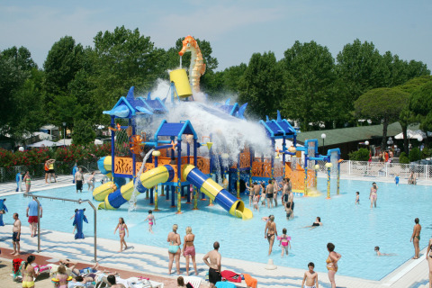 Families play in a colorful water park with slides and a giant water bucket at Camping Marina di Venezia, Italy.