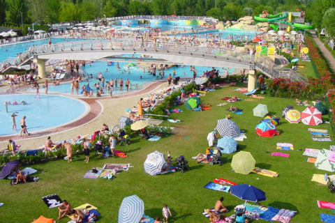 Crowded pool complex and grassy area with colorful umbrellas at Camping Village Marina di Venezia, Italy.