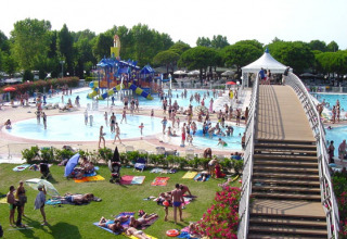 Levendig zwembad met glijbanen, ligweide en brug in Camping Village Marina di Venezia, Veneto, Italië.