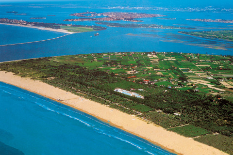 Vista aérea de Camping Village Marina di Venezia con campos verdes, playa de arena y mar azul en Véneto, Italia.
