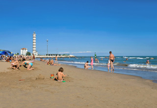 Beach scene at Camping Village Marina di Venezia, Veneto, Italy, with families, children, and a lighthouse.