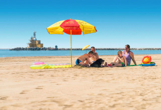 A family relaxes under a colorful beach umbrella at Camping Village Marina di Venezia in Veneto, Italy.