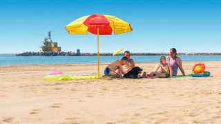 Una familia descansa bajo una sombrilla en la playa en Camping Village Marina di Venezia, Véneto, Italia.