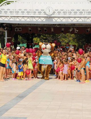 Niños y adultos reunidos alrededor de una mascota con globos en Camping Village Marina di Venezia en Italia.