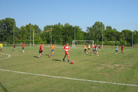 Kinderen spelen voetbal op een groene grasmat in Camping Village Marina di Venezia, Veneto, Italië, onder een blauwe hemel.