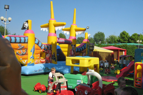 Children playing on a colorful playground with an inflatable pirate ship at Camping Village Marina di Venezia, Italy.