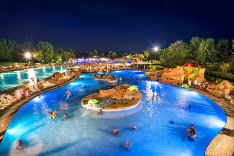 Piscina iluminada por la noche en Camping Village Marina di Venezia, Véneto, Italia, con visitantes felices.