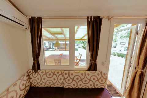 Vista interna dalla SunLodge Maple con divano, finestre e porta verso la terrazza al Camping Village Marina di Venezia.