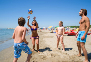 Family plays beach volleyball on the sandy shore at Camping Village Cavallino holiday park in Veneto, Italy.