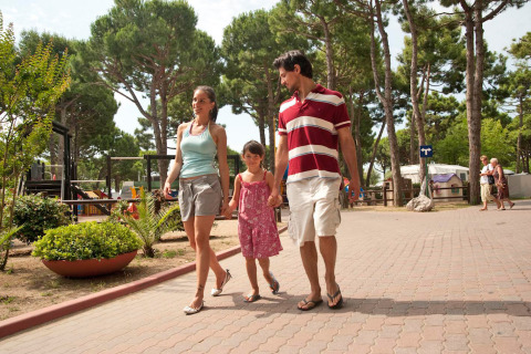 Famiglia che passeggia insieme nel parco vacanze tra gli alberi di Camping Village Cavallino, Veneto, Italia.